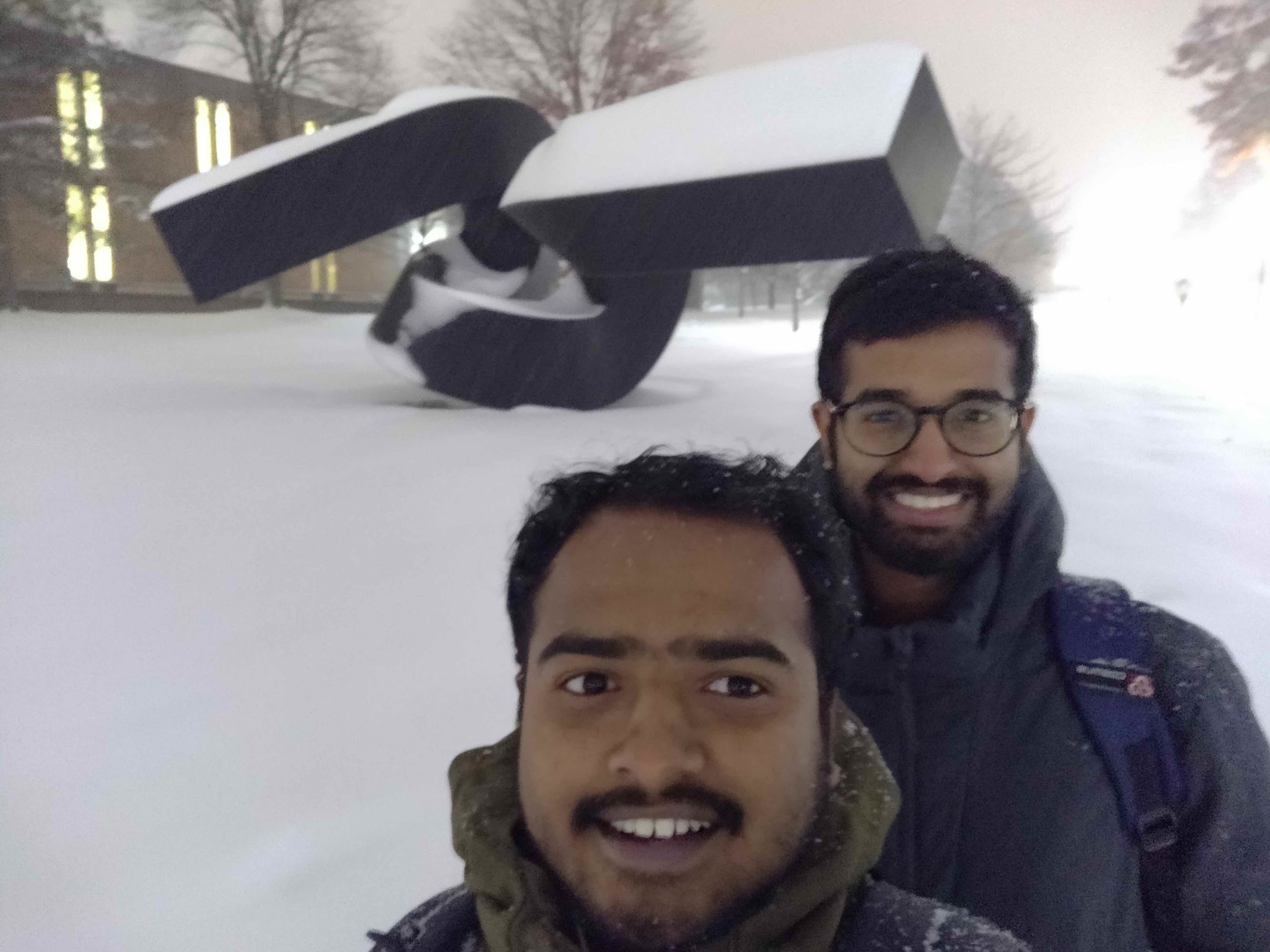Lakshmi Venkatesh Kakumani and friend in snow in front of sculptor on North Campus